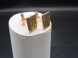un gros plan sur une paire de boucles d'oreilles à clous en or posées sur une boîte blanche