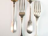 five silver spoons and two silver forks on a white surface