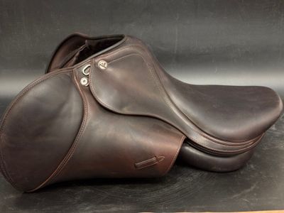 brown leather horse saddles on a black surface with a wooden stick
