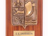 une plaque en bois sur laquelle figurent un bateau et une fleur, avec en dessous une autre plaque portant l'inscription « e e vauguelin »