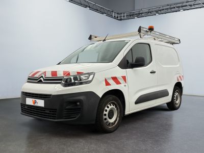 La camionnette blanche est garée dans une grande pièce ; elle porte une bande rouge et blanche sur le côté.