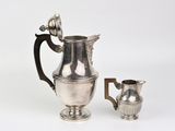 a silver pitcher and a silver cup on a white surface