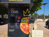 un distributeur automatique sur lequel est posée une pizza, au milieu d'un parking