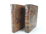 two old books are sitting side by side on a white surface