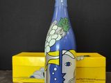 une bouteille bleue décorée d'une peinture, à côté d'une boîte jaune