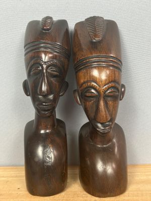une paire de sculptures africaines représentant des têtes, posées sur une étagère en bois