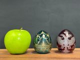 three different colored eggs sitting next to an apple
