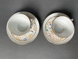 two cups and saucers with floral designs on them on a table