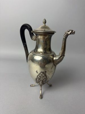 une théière ancienne en argent avec une poignée noire sur une surface blanche