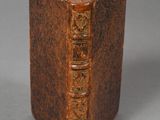 an old brown book sitting on top of a table next to a cup