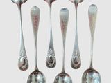 six cuillères en argent sont alignées sur une surface blanche