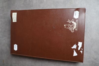 une valise marron recouverte d'autocollants, posée contre un mur
