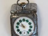une petite horloge en argent avec un cadran vert, posée sur une table
