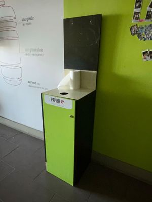 une poubelle verte et noire près d'un mur blanc