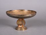 a silver bowl on a pedestal on a gray surface