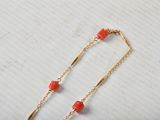 necklace with red beads and gold chain on a white surface