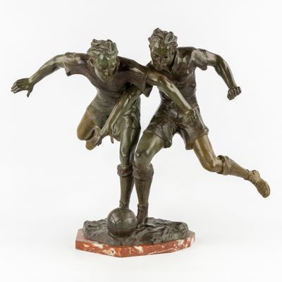 une photo d'une statue en bronze représentant deux hommes jouant au football
