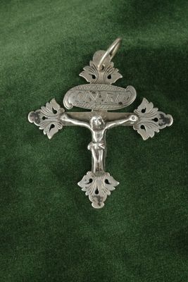 une croix posée sur un tissu vert, surmontée d'une croix en argent