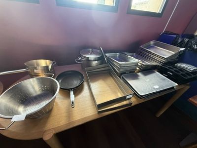 Plusieurs casseroles et poêles sont posées sur une table en bois dans une cuisine