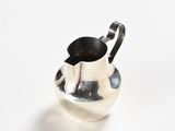 a silver pitcher with a handle on a white surface