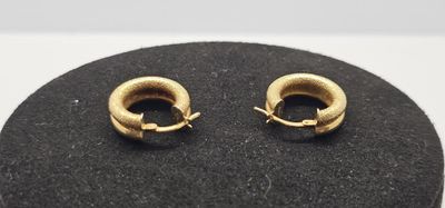 une paire de boucles d'oreilles créoles en or posées sur une surface noire