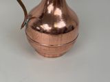 a copper pitcher with a handle on a white table
