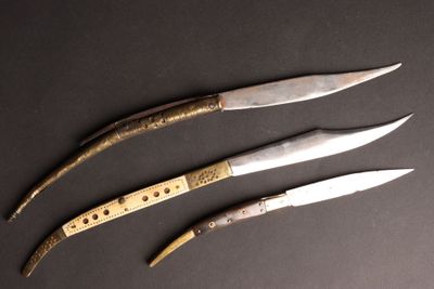 trois couteaux sont posés sur une surface noire, avec un manche en bois