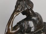 bronze statue of a boy sitting on a rock with his hand on his head