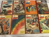 Plusieurs bandes dessinées sont alignées sur un lit recouvert d'un drap blanc.