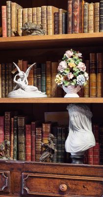 une bibliothèque sur laquelle sont posés de nombreux livres et un vase contenant des fleurs