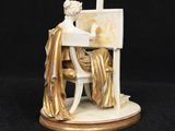 an antique figurine of a woman sitting at a desk in front of a painting easel
