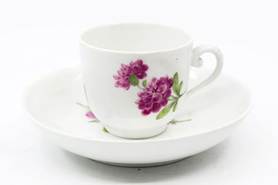 a white cup and saucer with purple flowers on it