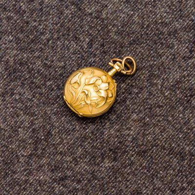 une image représentant une montre de poche en or posée sur une surface grise