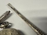 a silver pocket watch and a silver pen on a table