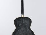 an old black acoustic guitar hanging on a white wall
