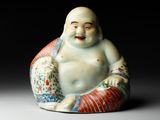 une petite statue représentant un Bouddha souriant, assis sur un coussin
