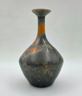 un vase noir et orange posé sur une surface blanche