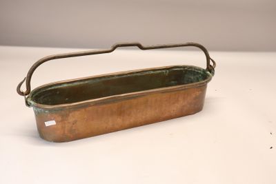 une vieille casserole en cuivre avec une poignée, posée sur une surface blanche