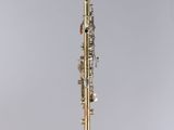 a gold plated clarinet on a stand with a white background