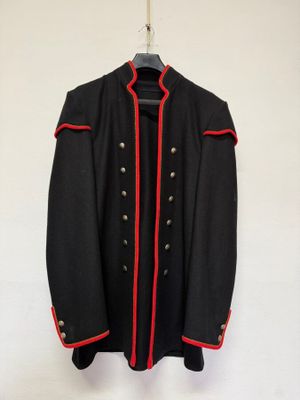 une veste noire aux bordures rouges accrochée à un mur blanc