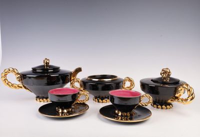 three black and gold tea cups and saucers on a white table
