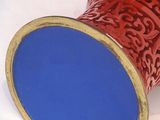a red vase with a blue lid sitting on a white surface