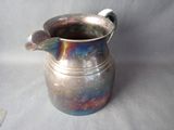 a silver pitcher sitting on a table next to a spoon