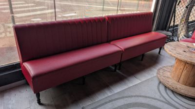 a red couch sitting in front of a window next to a wooden table