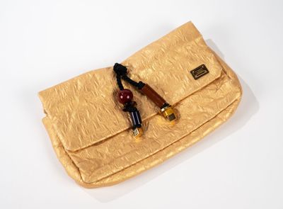 un sac à main doré muni d'une poignée en bois, posé sur une surface blanche
