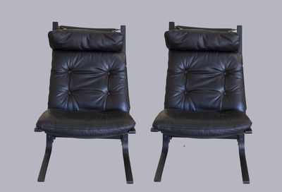 une paire de fauteuils de salon en cuir noir avec des pieds en métal noir