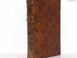 an old brown book with gold trim sitting on a white surface