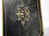 an old black book with gold writing on it sitting on a white surface