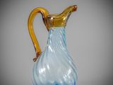a blue glass pitcher with a gold handle sitting on a table