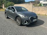 une Audi QX grise garée sur un parking près d'un mur de briques